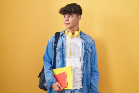 Foto de Adolescente hispana usando mochila de estudiante y sosteniendo libros sonriendo mirando al costado y mirando hacia otro lado pensando. - Imagen libre de derechos