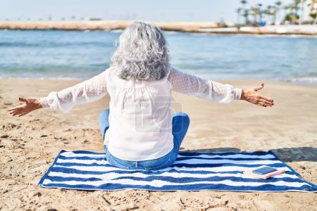 Foto de Mujer de mediana edad sentada sobre una toalla en la playa - Imagen libre de derechos