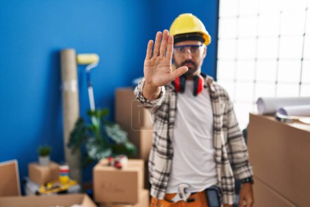 Photo for Young hispanic man with beard working at home renovation doing stop sing with palm of the hand. warning expression with negative and serious gesture on the face. - Royalty Free Image