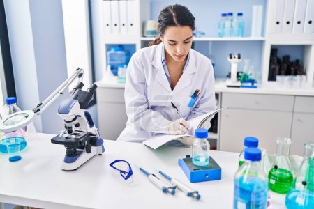 Photo for Young hispanic woman wearing scientist uniform measuring liquid at laboratory - Royalty Free Image