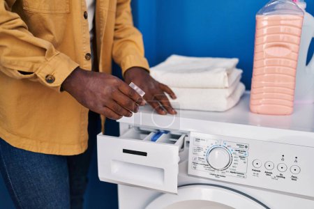 Photo for Young african american man smiling confident pouring detergent on washing machine at laundry room - Royalty Free Image