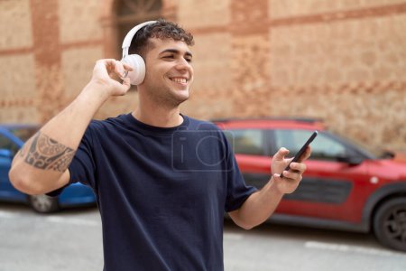 Téléchargez les photos : Jeune homme hispanique écoutant de la musique et dansant dans la rue - en image libre de droit