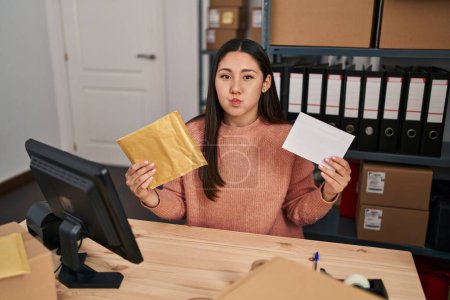 Photo for Young latin woman working at small business ecommerce packing order puffing cheeks with funny face. mouth inflated with air, catching air. - Royalty Free Image