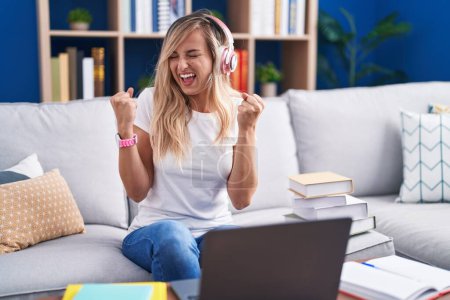 Téléchargez les photos : Jeune femme blonde étudiant à l'aide d'un ordinateur portable à la maison très heureuse et excitée de faire geste gagnant avec les bras levés, souriant et criant pour le succès. concept de célébration. - en image libre de droit