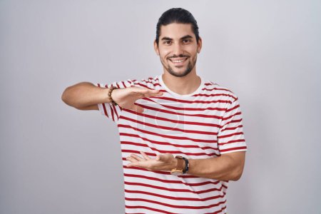 Photo for Hispanic man with long hair standing over isolated background gesturing with hands showing big and large size sign, measure symbol. smiling looking at the camera. measuring concept. - Royalty Free Image