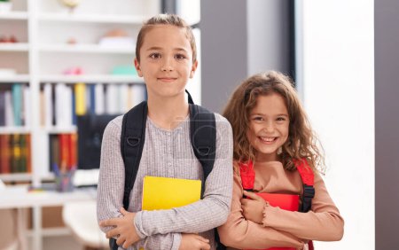 Foto de Two kids students wearing backpack holding book at classroom - Imagen libre de derechos
