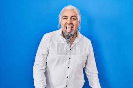 Photo for Middle age man with grey hair standing over blue background sticking tongue out happy with funny expression. emotion concept. - Royalty Free Image