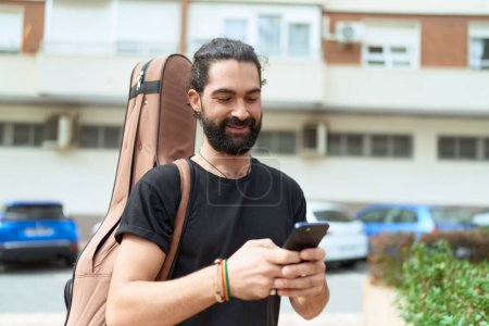Téléchargez les photos : Young hispanic man musician using smartphone holding guitar case at park - en image libre de droit