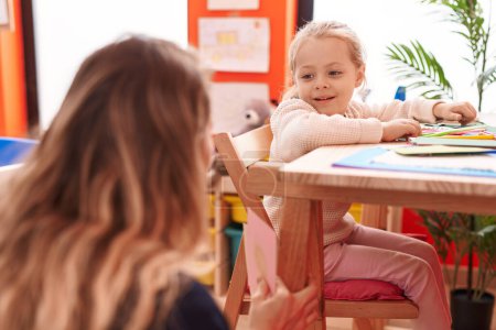 Foto de Maestro y niño pequeño sentado en la mesa teniendo una lección en el jardín de infantes - Imagen libre de derechos