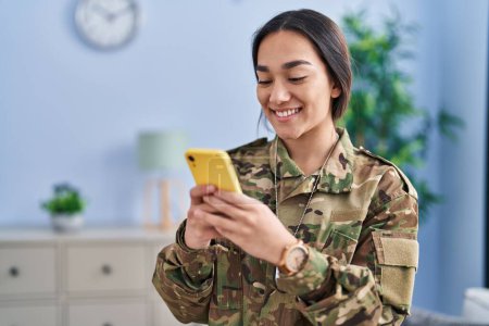 Téléchargez les photos : Jeune femme hispanique soldat de l'armée utilisant un smartphone à la maison - en image libre de droit