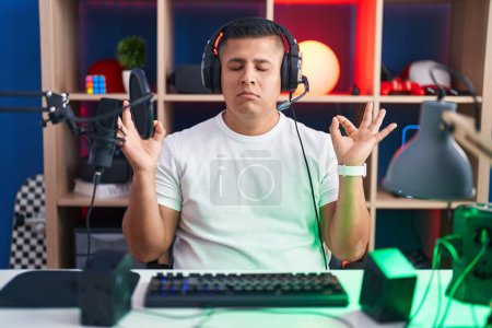 Téléchargez les photos : Young hispanic man playing video games relaxed and smiling with eyes closed doing meditation gesture with fingers. yoga concept. - en image libre de droit