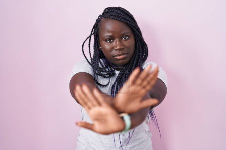 Téléchargez les photos : Jeune femme africaine debout sur fond rose expression de rejet croisement des bras et des paumes faisant signe négatif, visage en colère - en image libre de droit