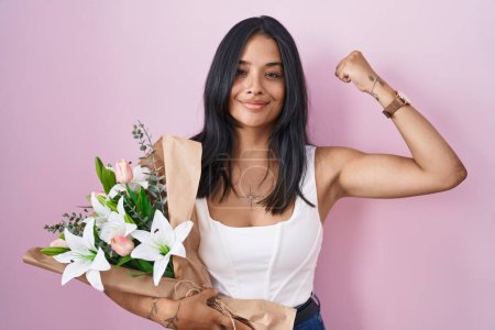 Foto de Brunette woman holding bouquet of white flowers strong person showing arm muscle, confident and proud of power - Imagen libre de derechos