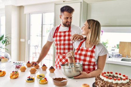 Téléchargez les photos : Jeune couple souriant cuisine confiante gâteau au chocolat à la cuisine - en image libre de droit