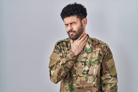 Foto de Arab man wearing camouflage army uniform touching painful neck, sore throat for flu, clod and infection - Imagen libre de derechos