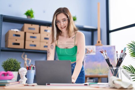 Photo for Young woman artist using laptop sitting on table at art studio - Royalty Free Image