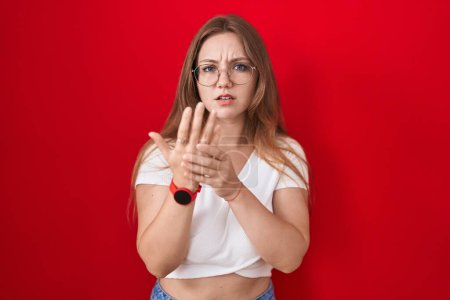 Photo for Young caucasian woman standing over red background suffering pain on hands and fingers, arthritis inflammation - Royalty Free Image