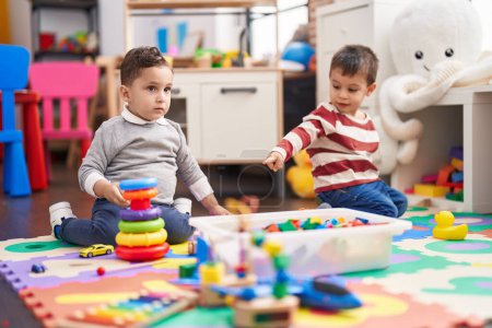 Foto de Two kids playing with toys sitting on floor at kindergarten - Imagen libre de derechos