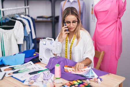 Téléchargez les photos : Young blonde woman tailor talking on smartphone choosing color at clothing shop - en image libre de droit