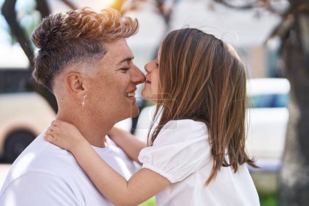 Foto de Padre e hija sonriendo confiados de pie juntos besando en el parque - Imagen libre de derechos