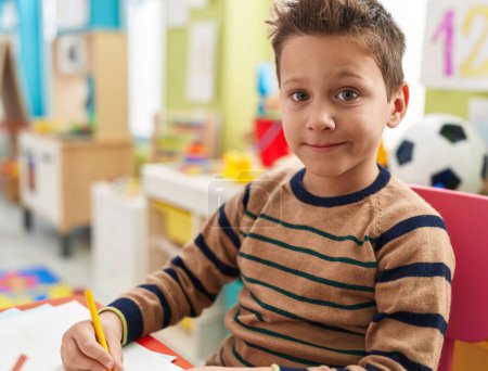 Photo for Adorable caucasian boy student sitting on table drawing on paper at kindergarten - Royalty Free Image