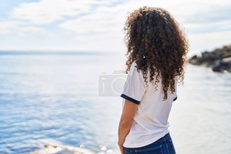 Foto de Young hispanic woman standing on back view at seaside - Imagen libre de derechos