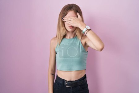 Photo for Blonde caucasian woman standing over pink background covering eyes with hand, looking serious and sad. sightless, hiding and rejection concept - Royalty Free Image