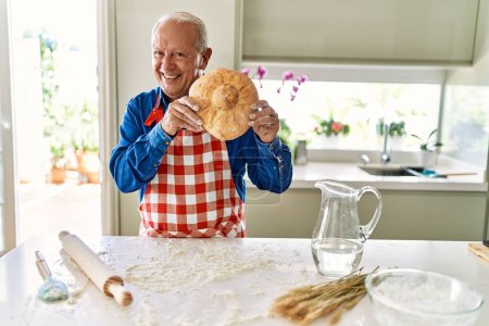 Photo for Senior man smiling confident holding homemade bread at kitchen - Royalty Free Image