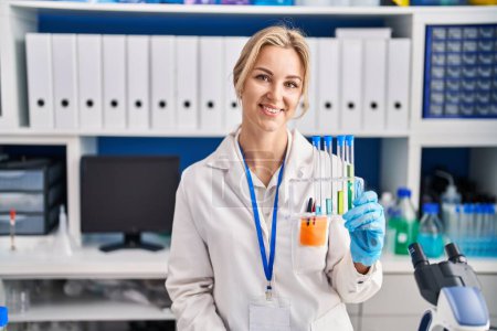 Photo for Young caucasian woman working at scientist laboratory holding test tubes looking positive and happy standing and smiling with a confident smile showing teeth - Royalty Free Image