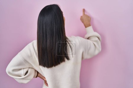 Foto de Young south asian woman standing over pink background posing backwards pointing ahead with finger hand - Imagen libre de derechos