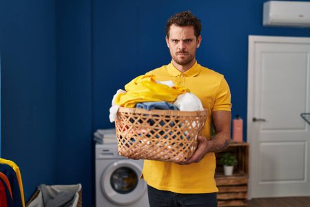 Téléchargez les photos : Young hispanic man holding laundry basket skeptic and nervous, frowning upset because of problem. negative person. - en image libre de droit