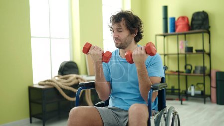 Téléchargez les photos : Young hispanic man sitting on wheelchair training with dumbbells at rehab clinic - en image libre de droit