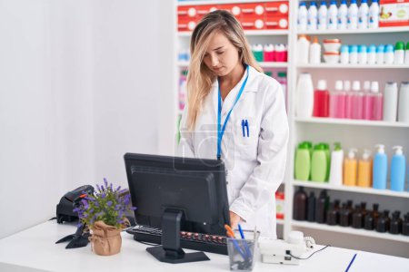 Téléchargez les photos : Young blonde woman pharmacist using computer at pharmacy - en image libre de droit