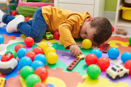Foto de Adorable chico caucásico jugando con el juguete del coche tirado en el suelo en el jardín de infantes - Imagen libre de derechos