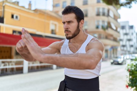 Photo for Young hispanic man karate fighter doing combat salute at street - Royalty Free Image