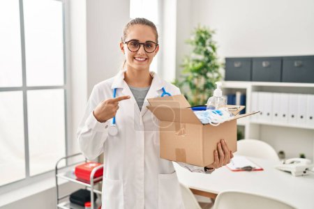 Photo for Young doctor woman holding box with medical items smiling happy pointing with hand and finger - Royalty Free Image
