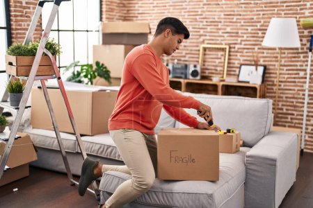 Téléchargez les photos : Young hispanic man unpacking cardboard box at new home - en image libre de droit