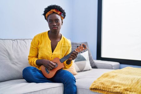 Téléchargez les photos : African young woman playing ukulele at home depressed and worry for distress, crying angry and afraid. sad expression. - en image libre de droit