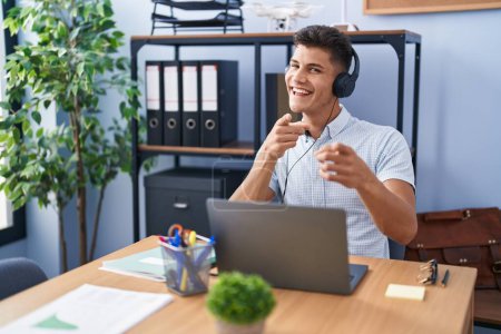 Photo for Young hispanic man working at the office wearing headphones pointing fingers to camera with happy and funny face. good energy and vibes. - Royalty Free Image