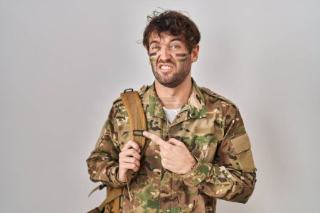 Foto de Hispanic young man wearing camouflage army uniform pointing aside worried and nervous with forefinger, concerned and surprised expression - Imagen libre de derechos