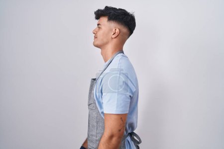 Photo for Hispanic young man wearing apron over white background looking to side, relax profile pose with natural face and confident smile. - Royalty Free Image