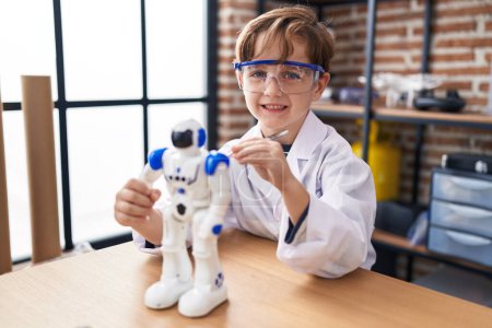 Téléchargez les photos : Adorable garçon hispanique étudiant souriant robot réparateur confiant à la salle de classe de laboratoire - en image libre de droit