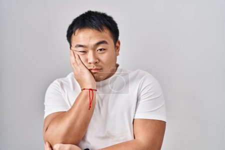 Téléchargez les photos : Jeune homme chinois debout sur fond blanc pensant fatigué et ennuyé avec des problèmes de dépression avec les bras croisés. - en image libre de droit