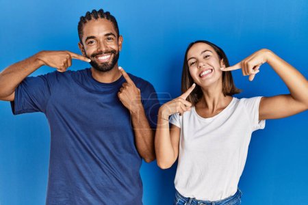 Téléchargez les photos : Young hispanic couple standing together smiling cheerful showing and pointing with fingers teeth and mouth. dental health concept. - en image libre de droit