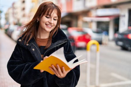 Téléchargez les photos : Jeune femme souriant livre de lecture confiant à la rue - en image libre de droit
