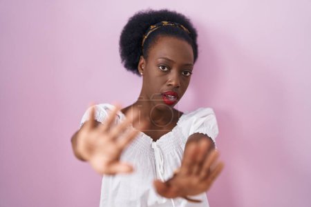 Téléchargez les photos : African woman with curly hair standing over pink background doing frame using hands palms and fingers, camera perspective - en image libre de droit
