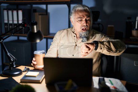 Photo for Middle age man with grey hair working at the office at night looking at the watch time worried, afraid of getting late - Royalty Free Image