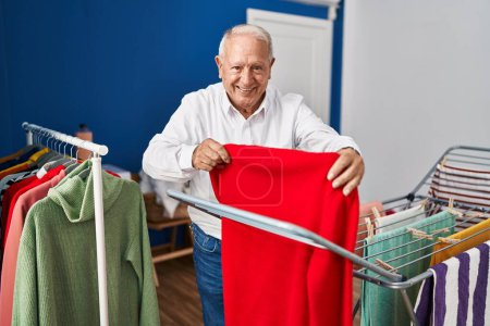 Foto de Hombre mayor sonriendo confiado colgando ropa en tendedero en la sala de lavandería - Imagen libre de derechos