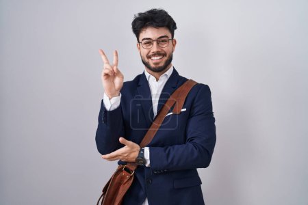 Téléchargez les photos : Hispanic man with beard wearing business clothes smiling with happy face winking at the camera doing victory sign with fingers. number two. - en image libre de droit