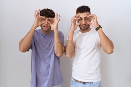 Téléchargez les photos : Homosexuel gay couple debout sur blanc fond essayer d'ouvrir les yeux avec doigts somnolent et fatigué pour matin fatigue - en image libre de droit